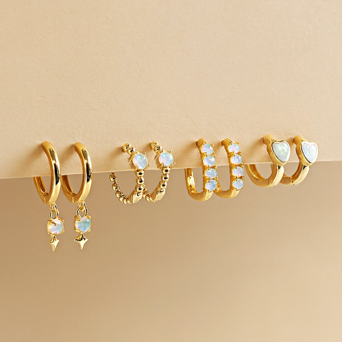 Set of gold opal huggie hoop earrings on a beige background from AMYO.