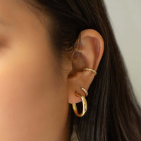 Close-up of woman wearing gold chunky hoops, moissanite crystal huggie, & rope beaded cuff. 