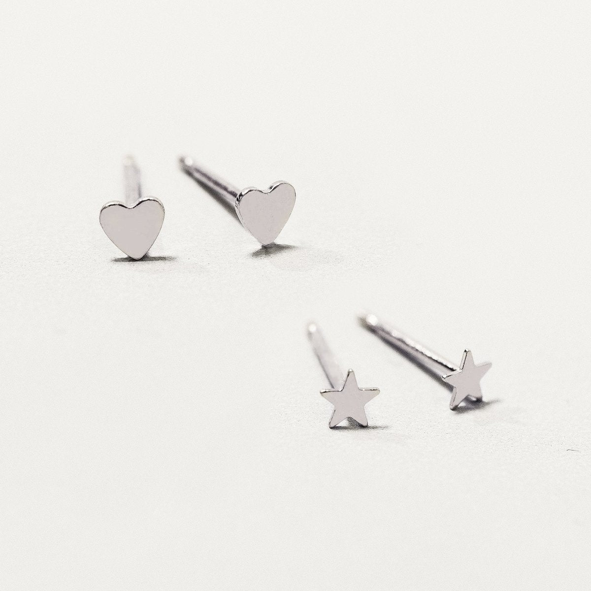 Sterling silver tiny heart and star studs scattered on a cream surface, close-up detail