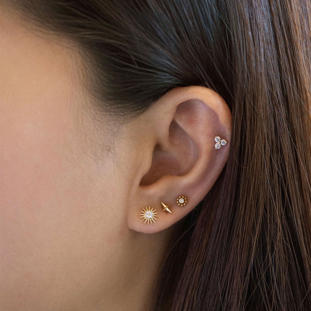 Close-up of an ear wearing multiple gold flat back earring styles from AMYO.