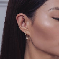 Woman wearing gold pave huggie earring and gold starburst huggie earrings 