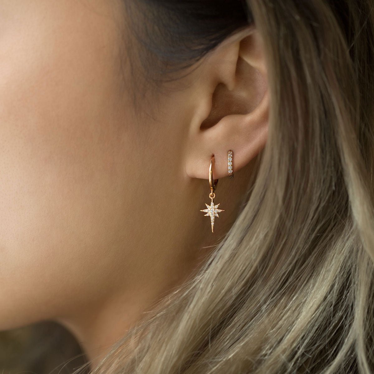 Close-up of woman wearing rose gold starburst huggie earring and rose gold pave huggie earring