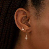 Close-up of woman wearing rose gold starburst huggie earring and rose gold crescent moon pave studs