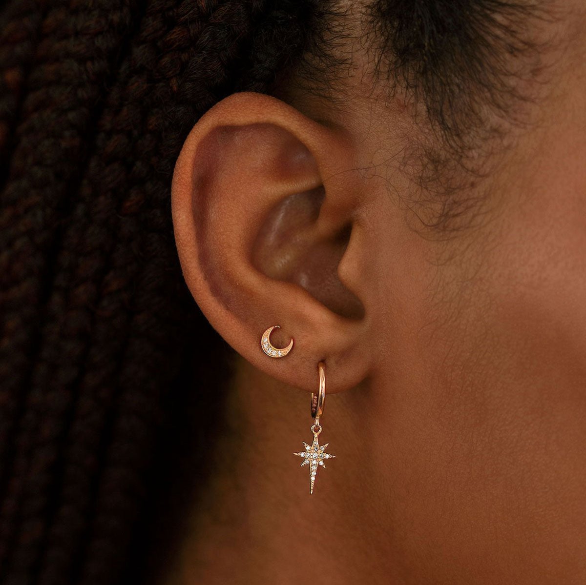 Close-up of woman wearing rose gold starburst huggie earring and rose gold crescent moon pave studs