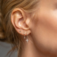 Close-up of woman wearing silver starburst huggie earring, silver star flare huggie earring, and silver tiny star stud