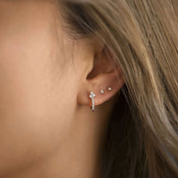 Close-up of woman's ear featuring Sterling Silver Clover Pave Huggie Earrings and silver studs. 