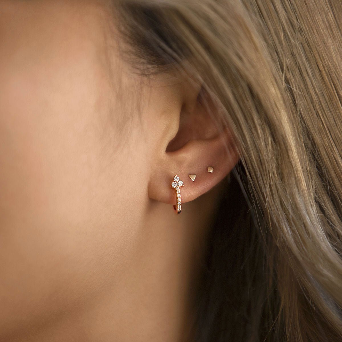 Close-up of woman's ear featuring Rose Gold Clover Pave Huggie Earrings and gold studs. 