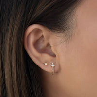 Close-up of woman's ear featuring Rose Gold Clover Pave Huggie Earrings  and gold stud. 