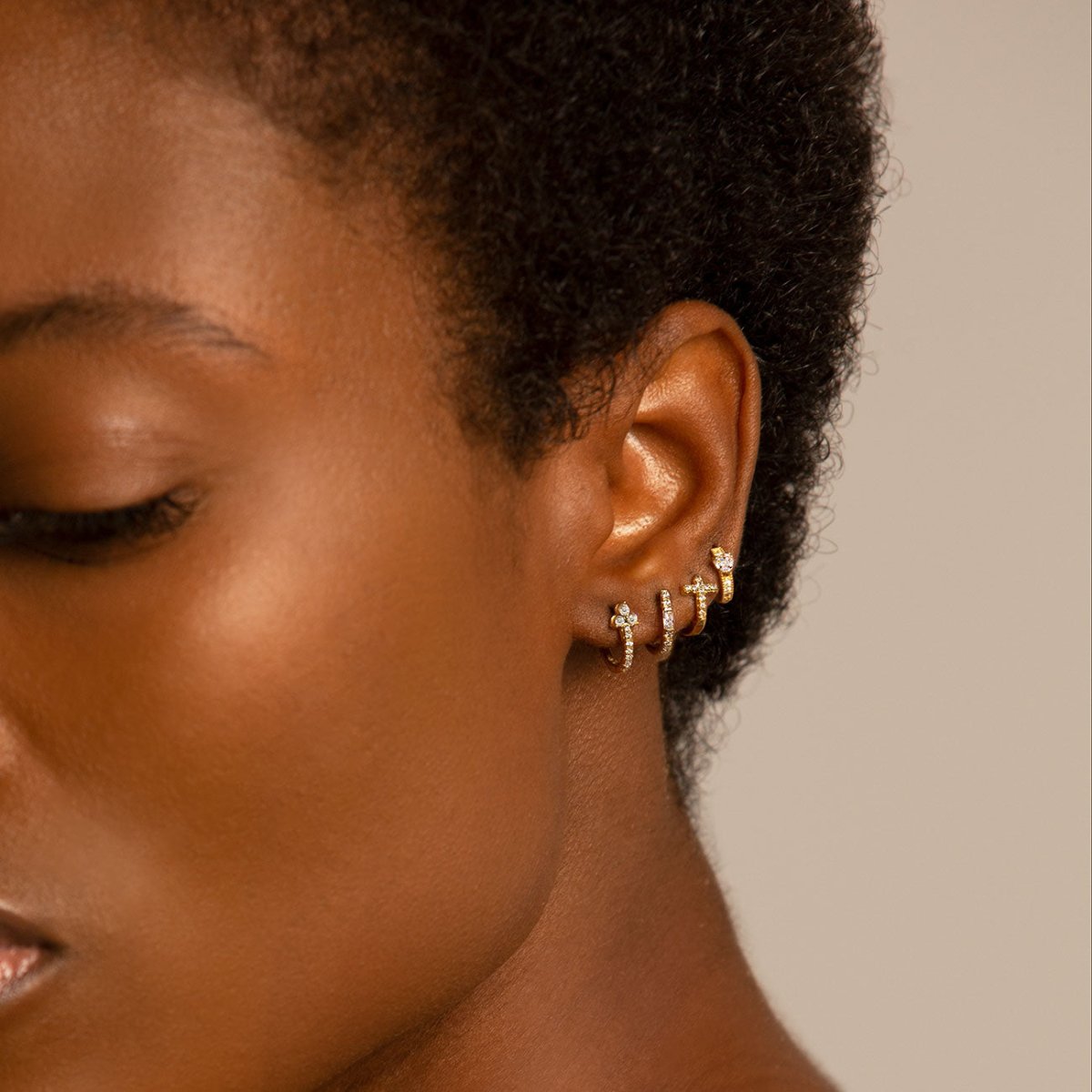 Close up of woman's ear featuring 14K Gold Tiny Heart Huggie Hoop Earring paired with other gold huggie earrings 