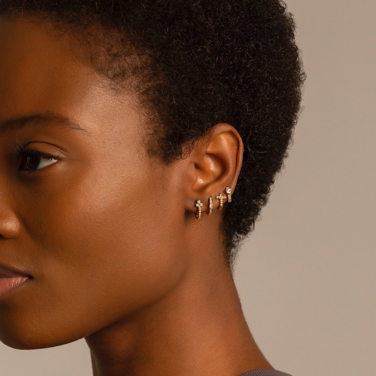 Close up of woman's side face featuring Gold Vermeil Tiny Heart Huggies paired with other gold huggies 