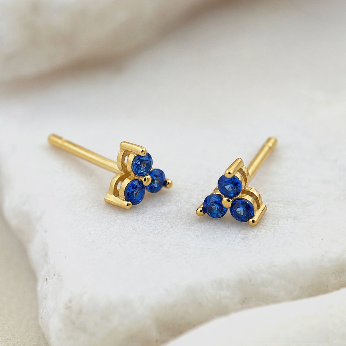 Pair of gold vermeil studs, each with three round blue stones in a clover cluster, on a white stone surface