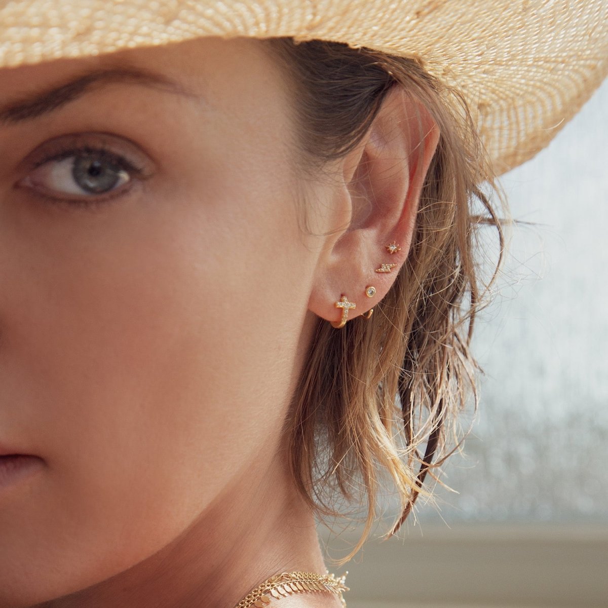 Model wearing tiny cross huggie earring, solitaire huggie, starburst and lightning bolt stud