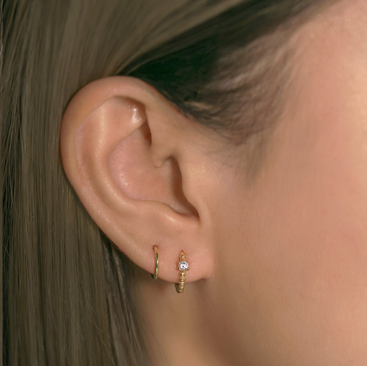 Close-up on woman's ear featuring Gold Vermeil Gemstone Bead Huggies White Zirconia CZ Crystal and gold huggie. 