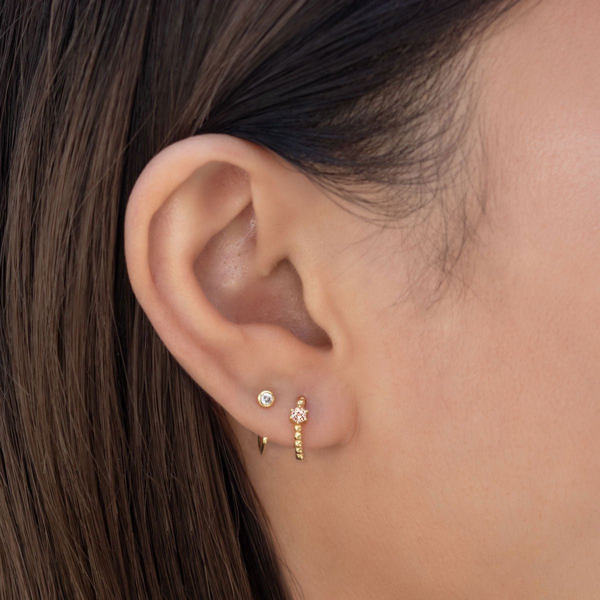 Close-up on woman's ear featuring the Gold Vermeil Gemstone Bead Huggies Pink CZ Crystal paired with tiny solitaire huggie earring. 