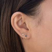 Close-up on woman's ear featuring the Gold Vermeil Gemstone Bead Huggies Blue Sapphire paired with tiny solitaire huggie earring. 