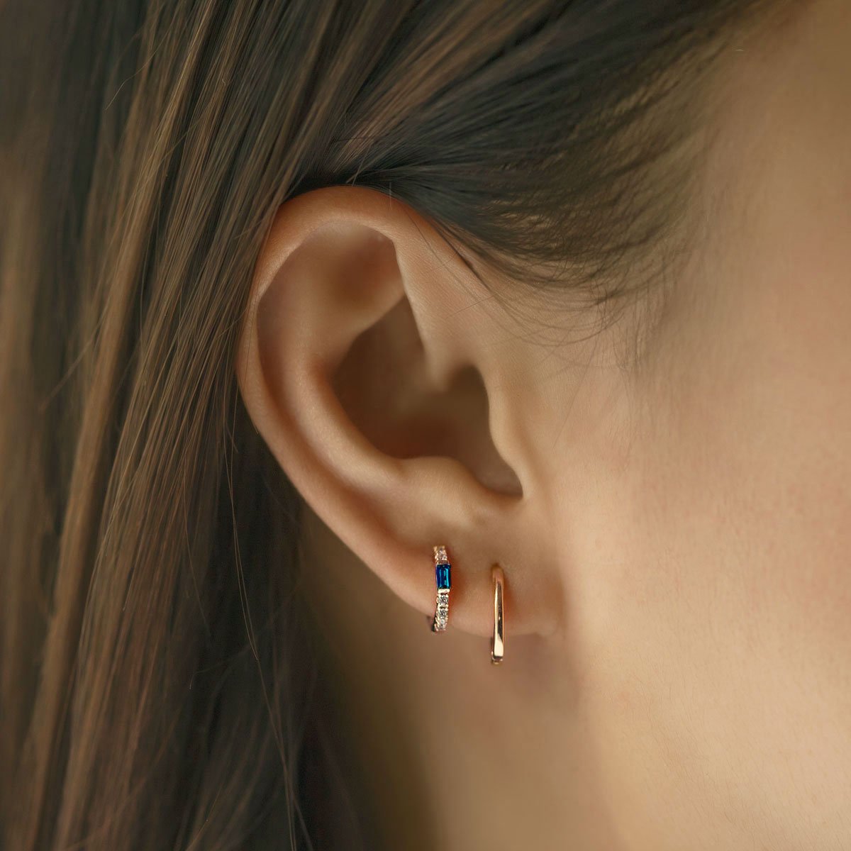 Close-up of woman's ear featuring Gold Vermeil Gemstone Baguette Huggie Earrings Blue Sapphire and gold hoop. 