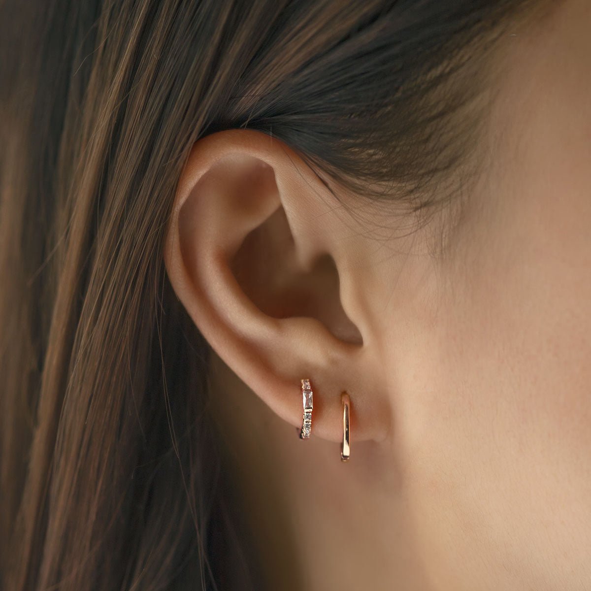 Close-up on woman's ear featuring Rose Gold Baguette Huggie Earrings CZ Crystal and rose gold hoop earrings. 