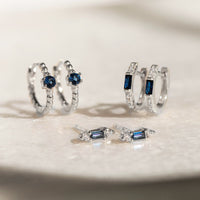 Close-up of earrings featuring Sterling Silver Gemstone Baguette Huggie Earrings Blue Sapphire and other crystal earrings. 