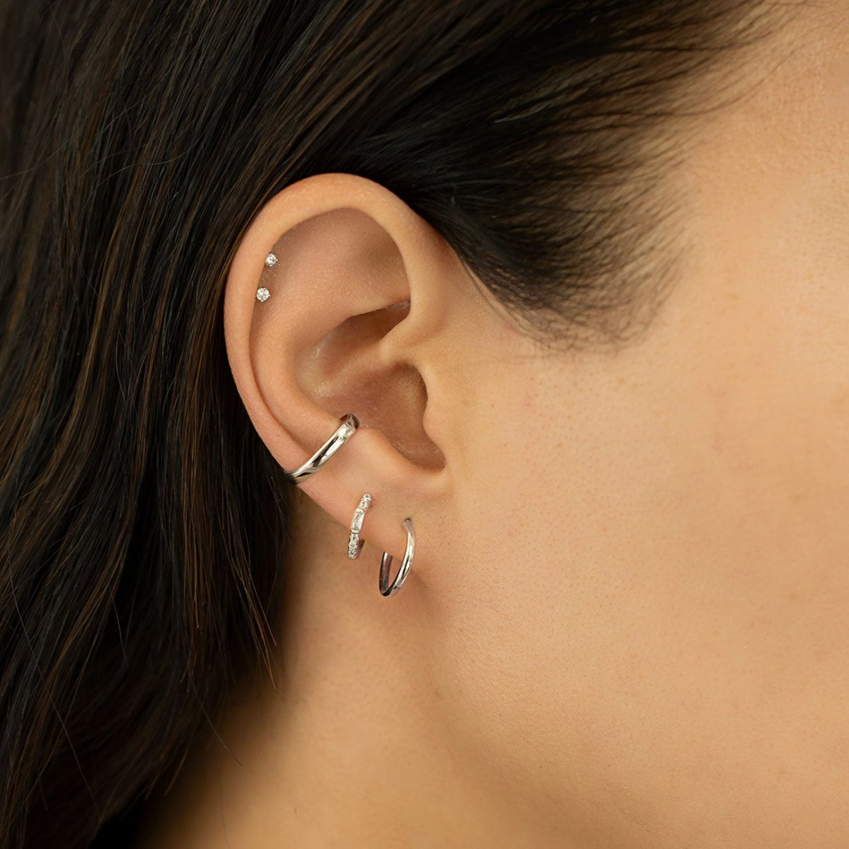 Close-up of woman's ear featuring Tiny 14K White Gold Crystal Stud Earrings paired with huggie earrings and cuff 