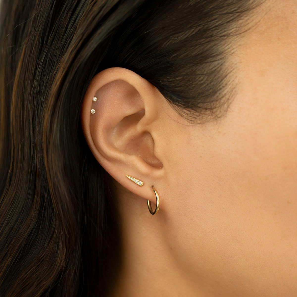 Close-up of woman's ear featuring Gold Filled Thin Huggie Hoops and 14K Tiny Sapphire Studs