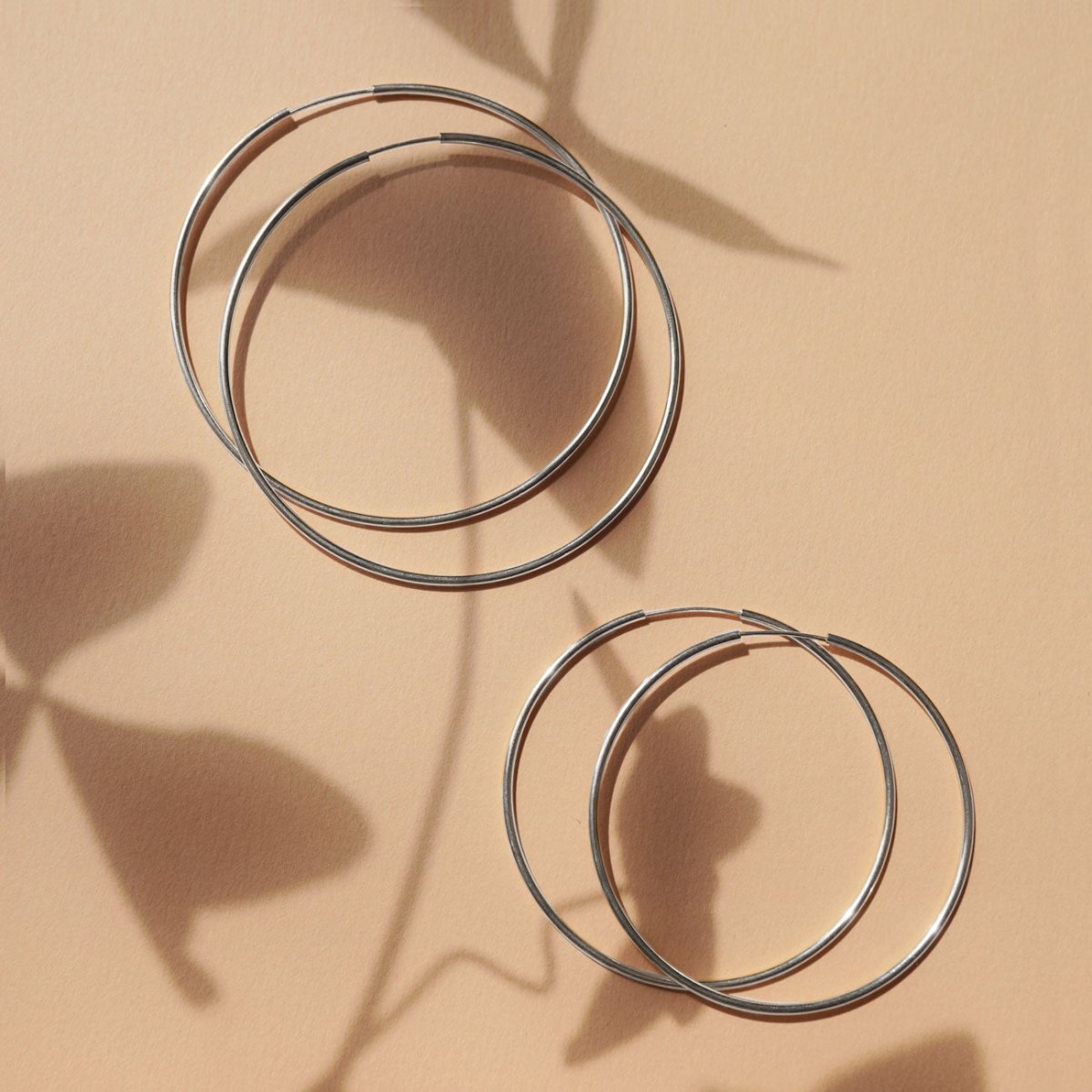 Close-up on earrings featuring Sterling Silver Thin Large Hoops and Sterlign Silver Midi Hoop Earrings. 