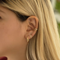 Model wearing midi gold hoop earrings, gold pave huggie hoops, and gold eternity and pavé ear cuff set