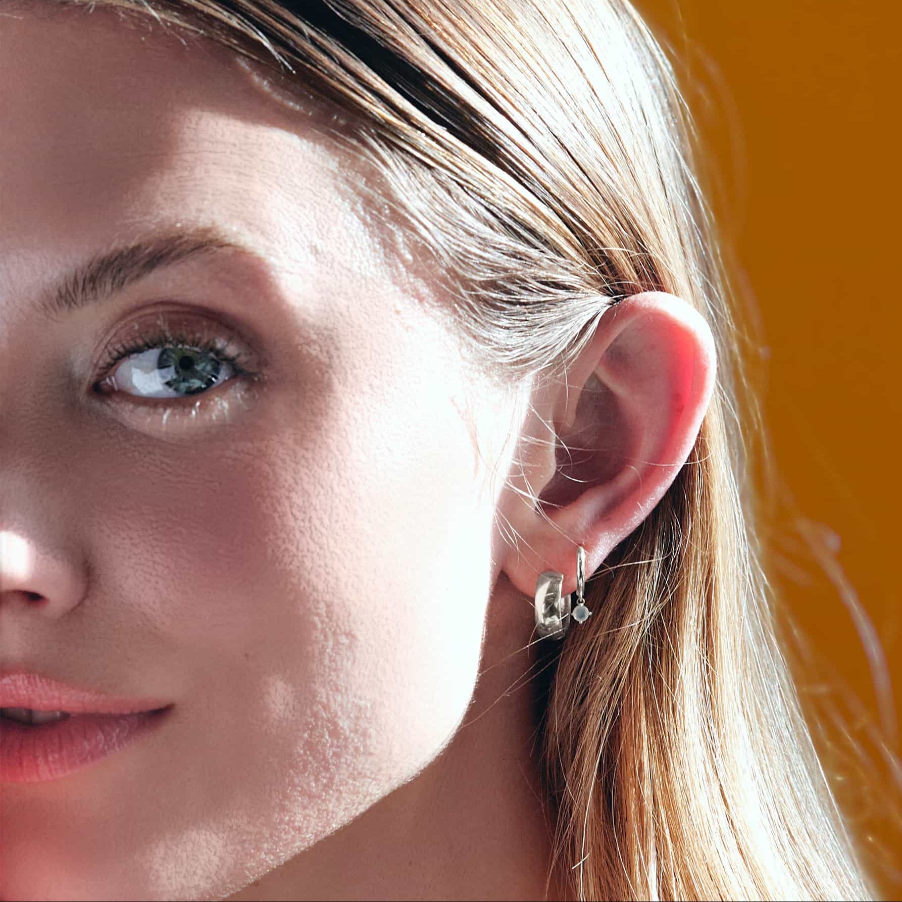 Close-up of woman's ear featuring 14K White Gold Gemstone Dangle Huggies Moissanite and Boyfriend Mini Hoops 