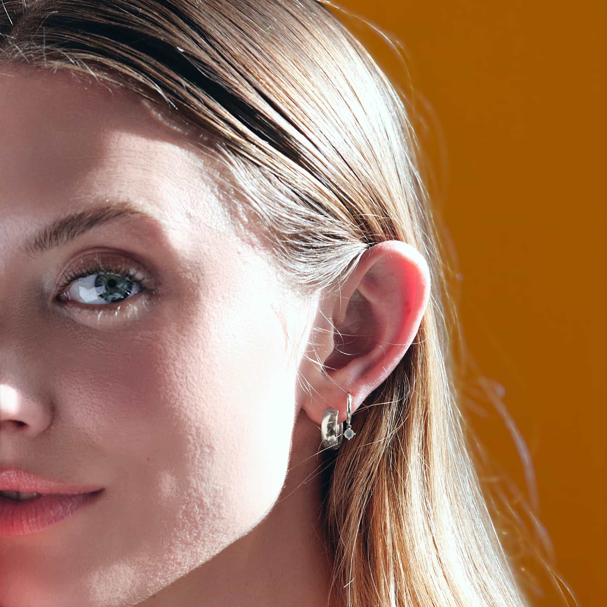 Close-up of woman's ear featuring 14K White Gold Gemstone Dangle Huggies Moissanite and Boyfriend Mini Hoops 