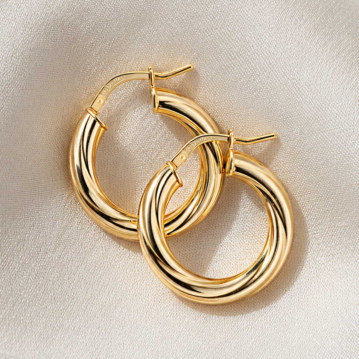 Pair of thick twisted gold vermeil hoop earrings with hinged closures, overlapping on cream fabric