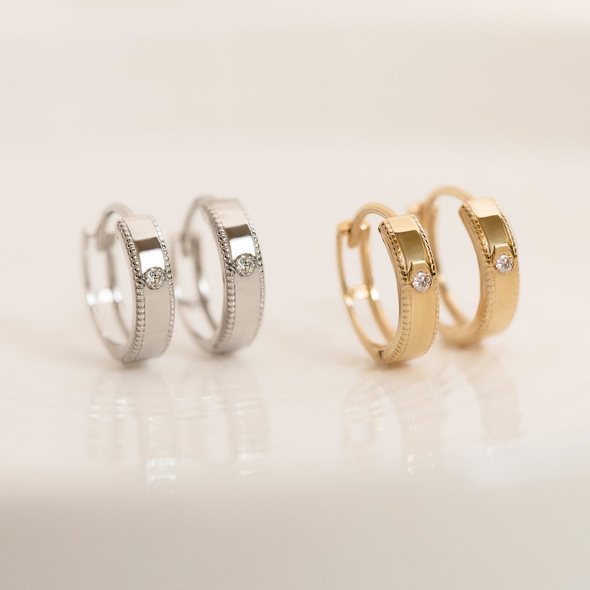 Sterling silver and gold vermeil milgrain solitaire huggie hoops with round zirconia, on a cream background