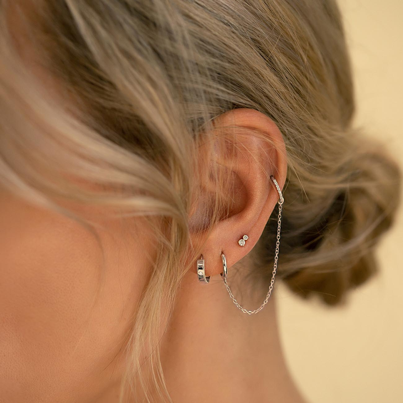 Sterling silver milgrain band huggie with a clear stone, shown on a model's lobe with a paved hoop