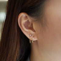 Close-up of woman's ear featuring 14K Gold Tiny Sapphire and Chain Studs paired with solitaire baguette diamond hoops 