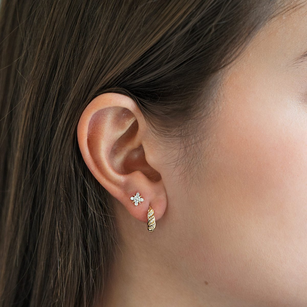 Close-up of an ear wearing AMYO's Mini Diamond Croissant Huggie Earrings and Diamond Starburst Stud Earrings