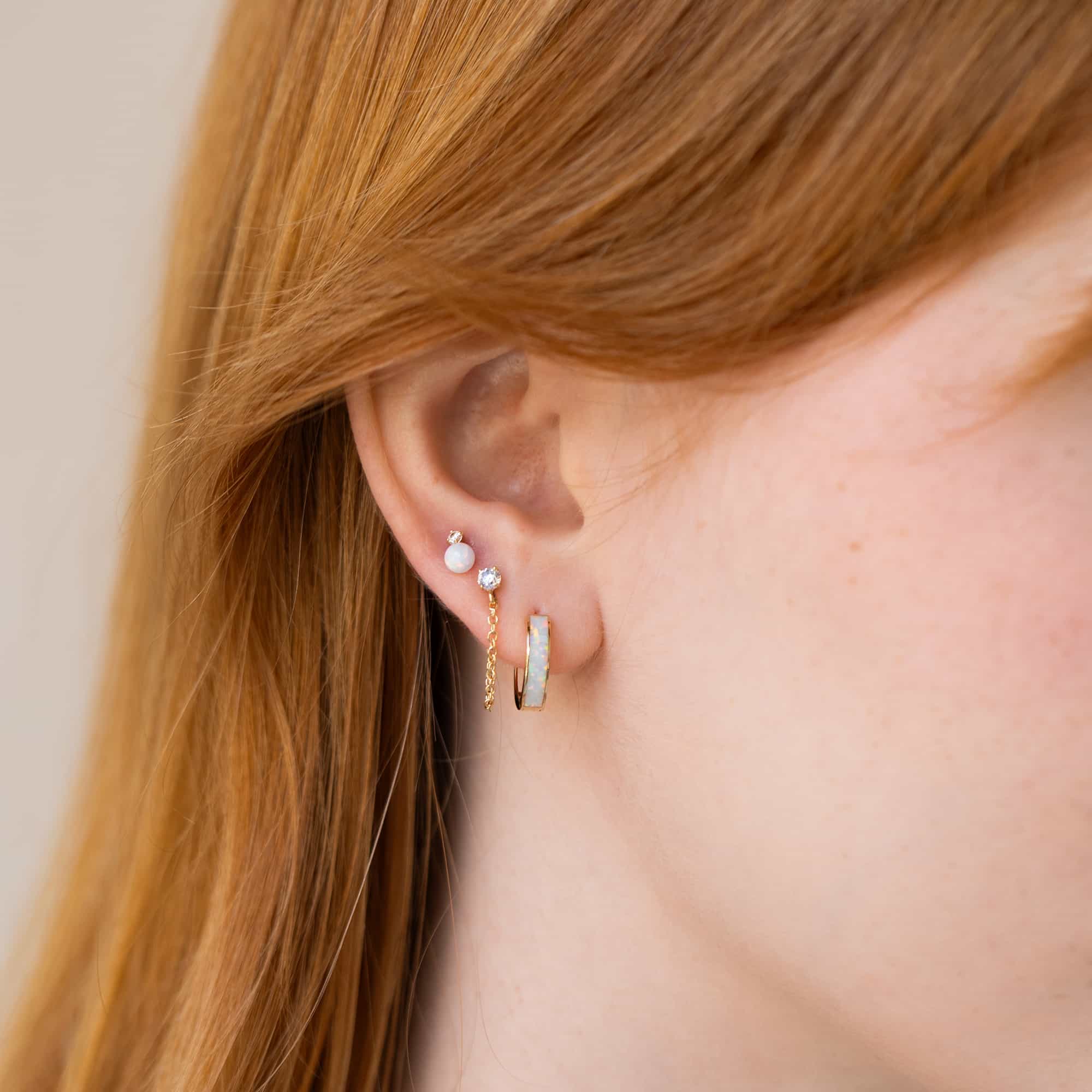 Close-up of woman's ear featuring 14K Gold Tiny Sapphire and Chain Studs paired with opal earrings 