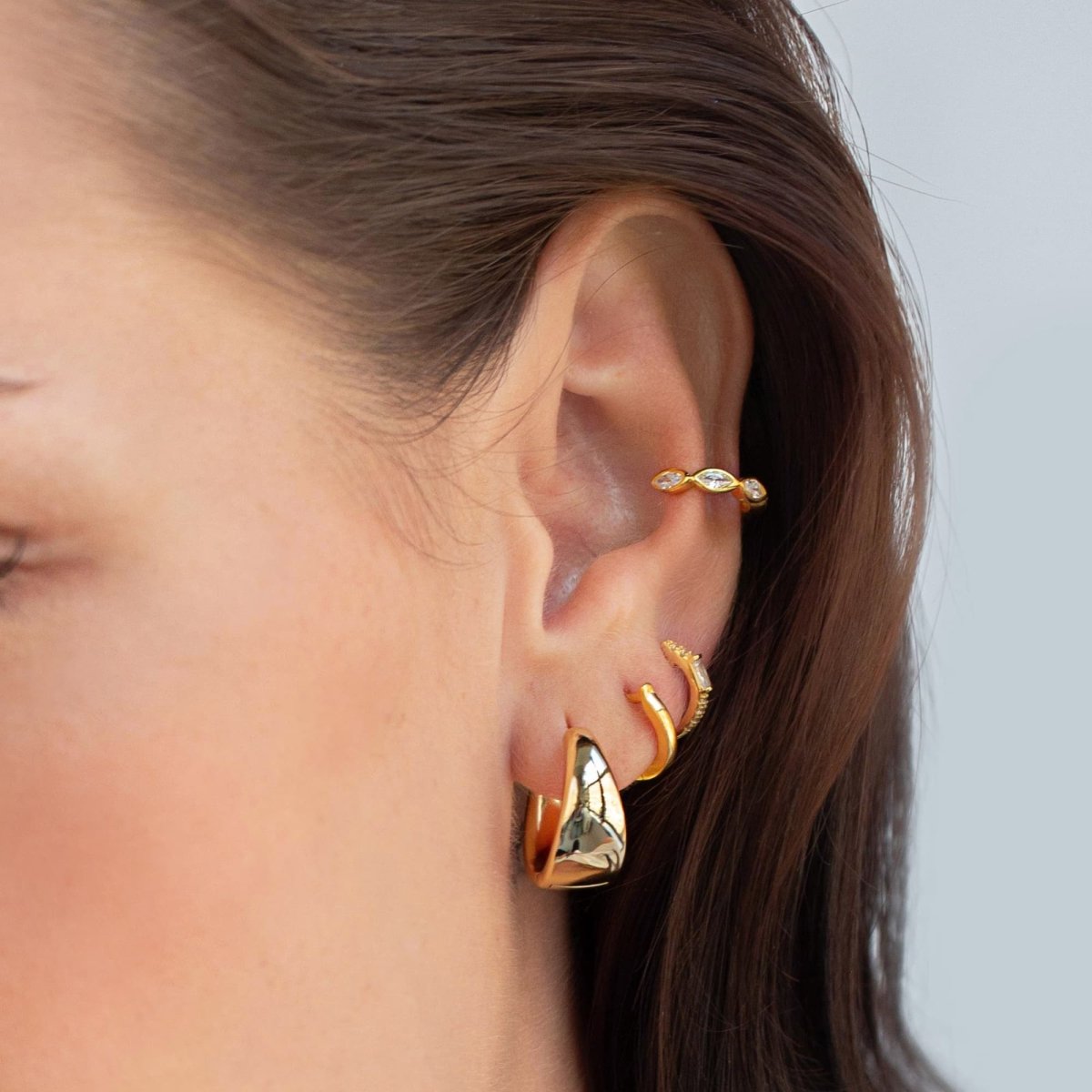 Close-up on woman's ear stack featuring Gold Vermeil Baguette Huggie Earrings CZ Crystal, chunky gold hoops, and gold cuff. 