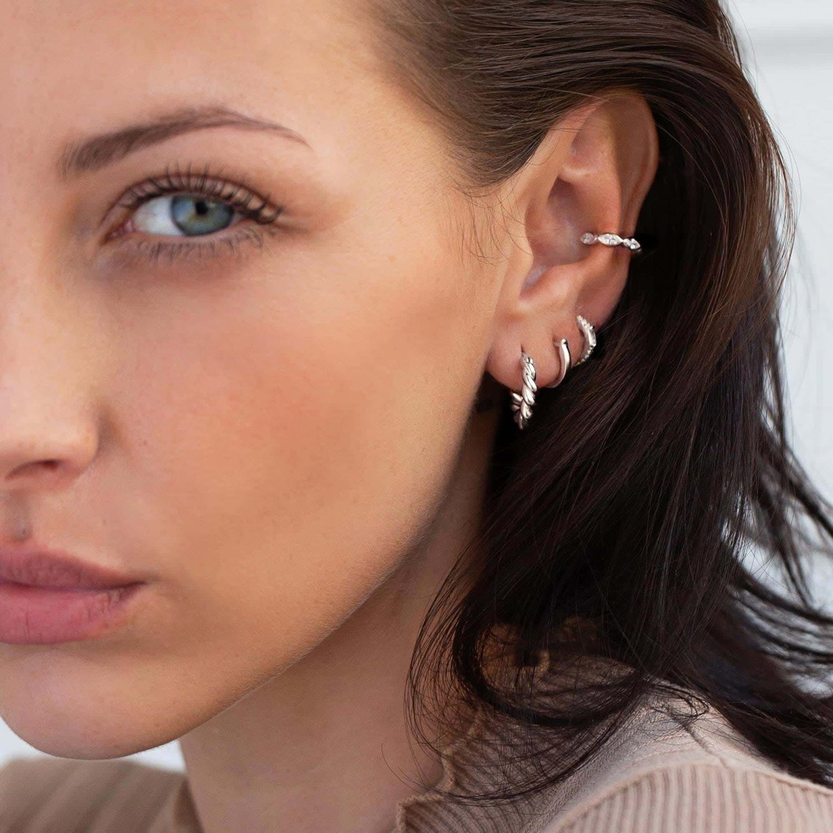 Close-up on woman's ear stack featuring Sterling Silver Baguette Huggie Earrings CZ Crystal, rope twisted silver hoops, and silver cuff. 