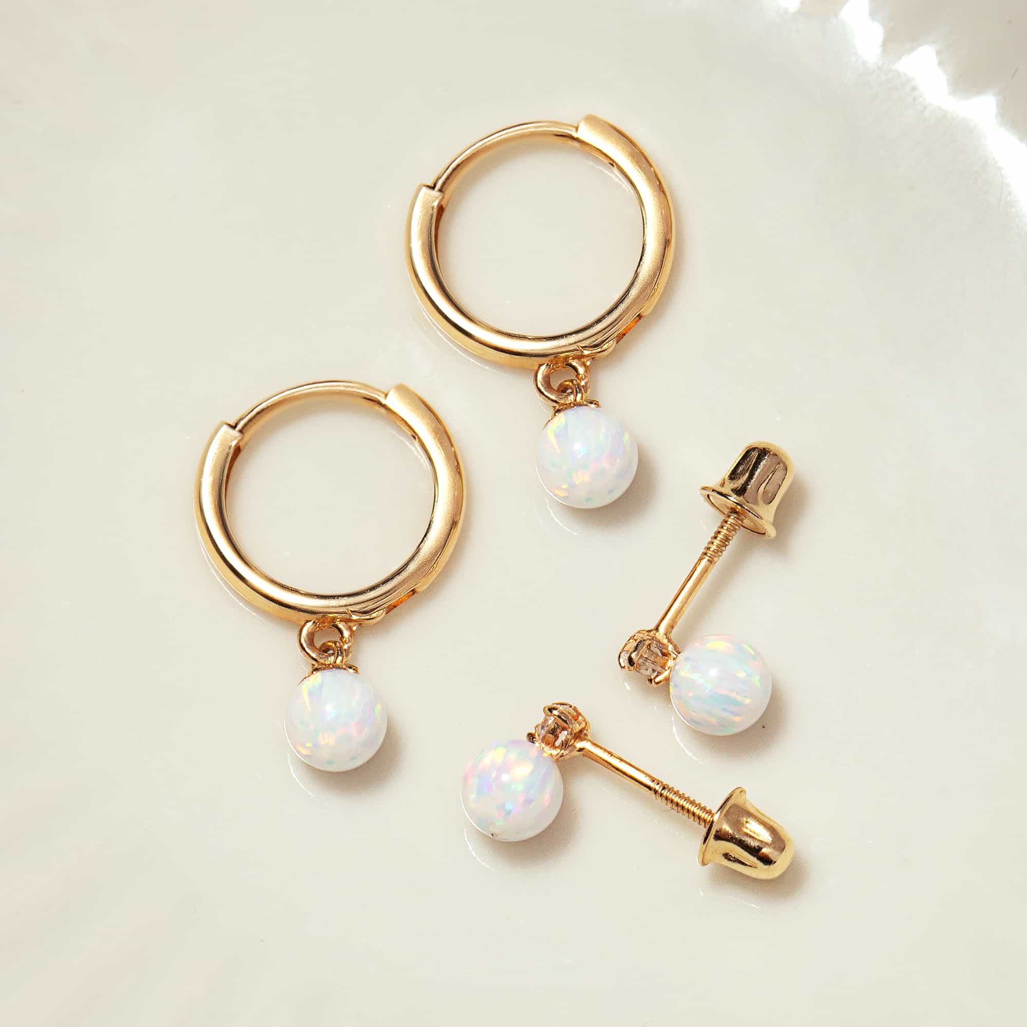 Close-up of earring featuring 14K Gold Tiny Opal Huggies and stud earrings