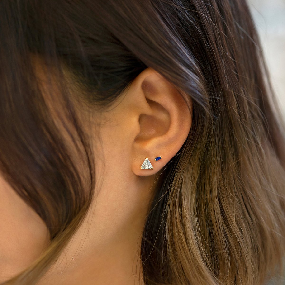 14K gold blue sapphire baguette stud, shown on a model's lobe beside a triangle clear-stone stud