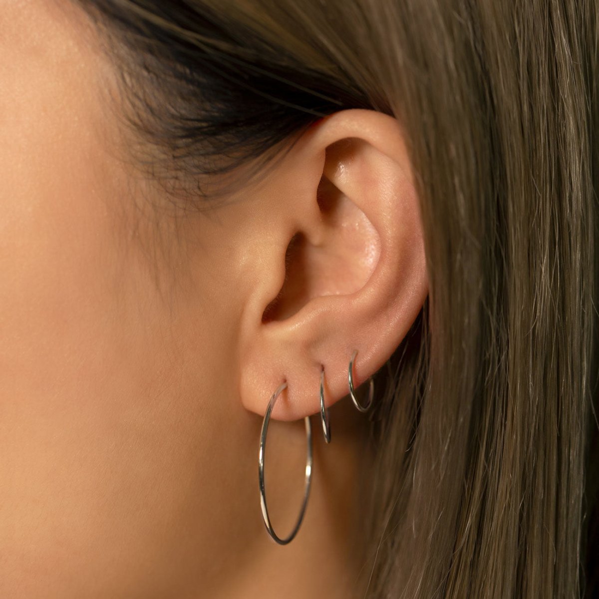 Close-up of woman's ear featuring 14K White Gold Thin Midi Hoops and Small Hoops 