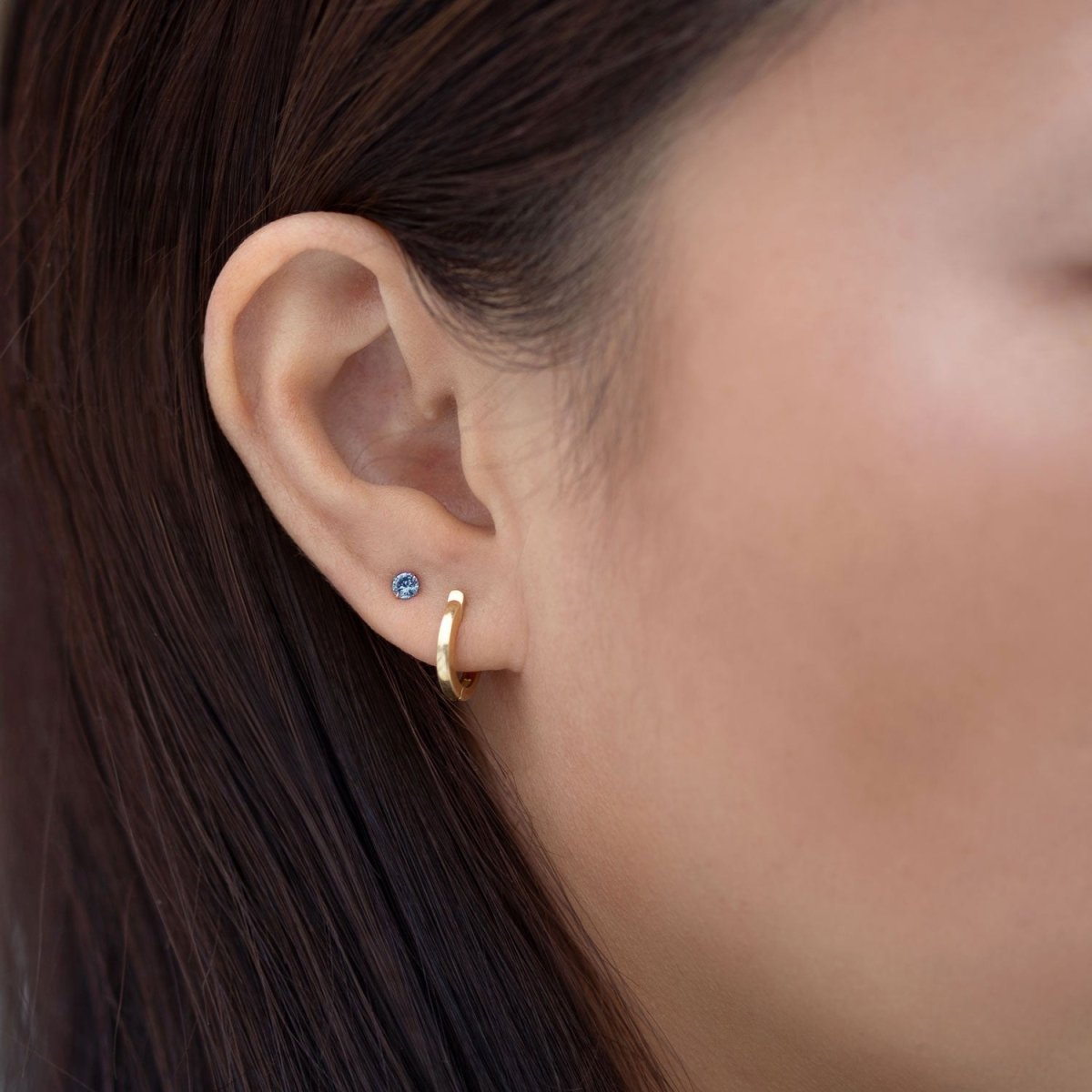 Close-up of woman's ear featuring 14K Gold Birthstone Tiny Studs Blue Zircon paired with huggie earring 