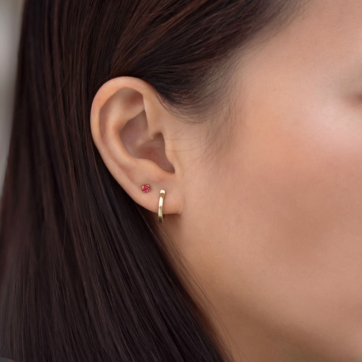 Close-up of woman's ear featuring 14K Gold Birthstone Tiny Studs Garnet and huggie earring