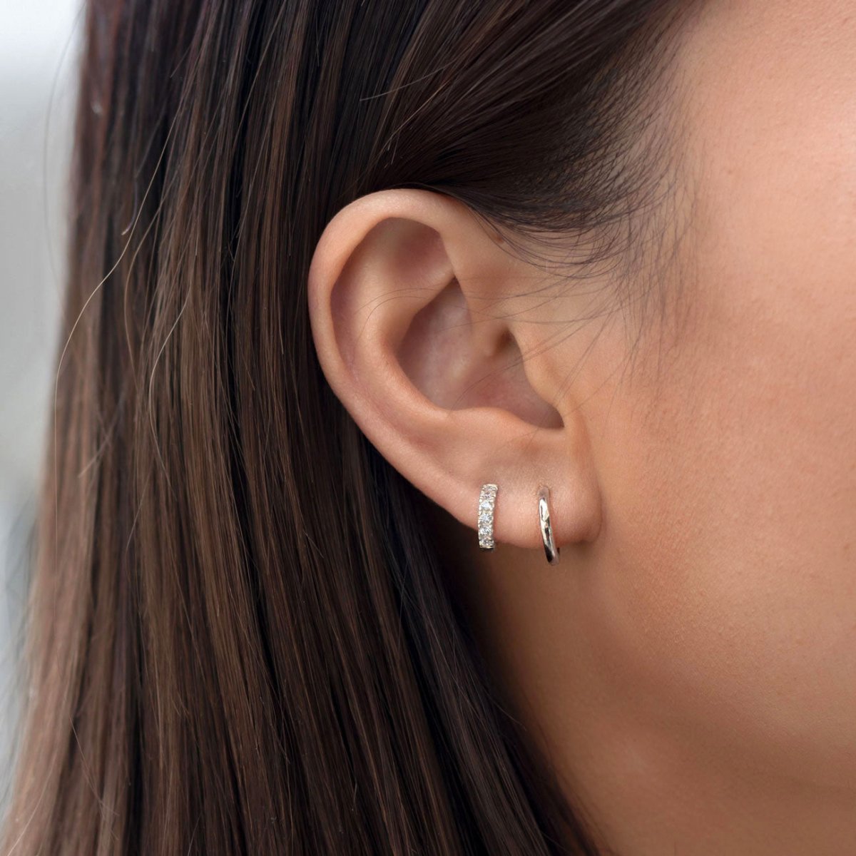 Close-up of woman's ear featuring 14K white gold moissanite crystal pave huggie earring and 14K gold pave huggie. 