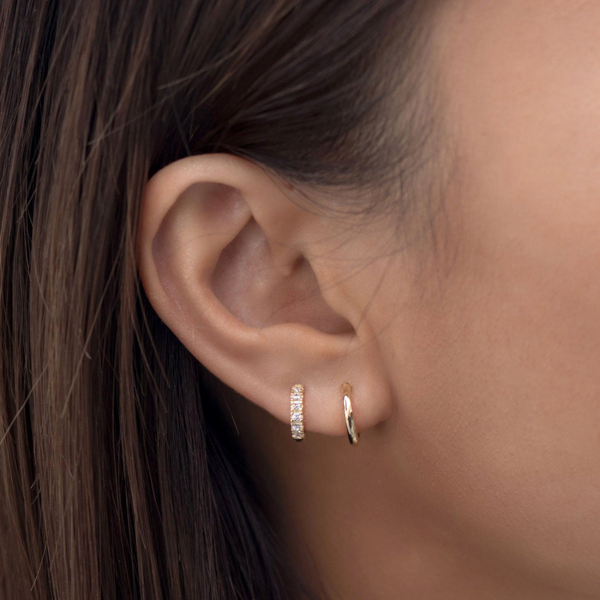 Close-up of woman's ear featuring 14K gold moissanite crystal pave huggie earring and 14K gold pave huggie. 