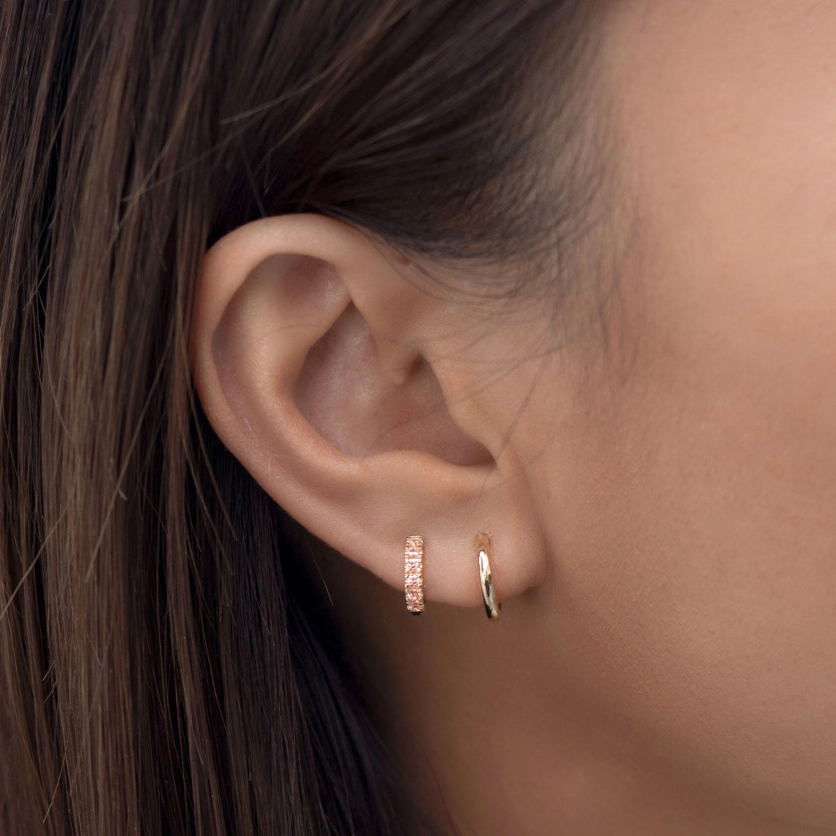 Close-up of woman's ear featuring 14K Gold Gemstone Pavé Huggies Pink and 14K gold pavé huggie earrings.  