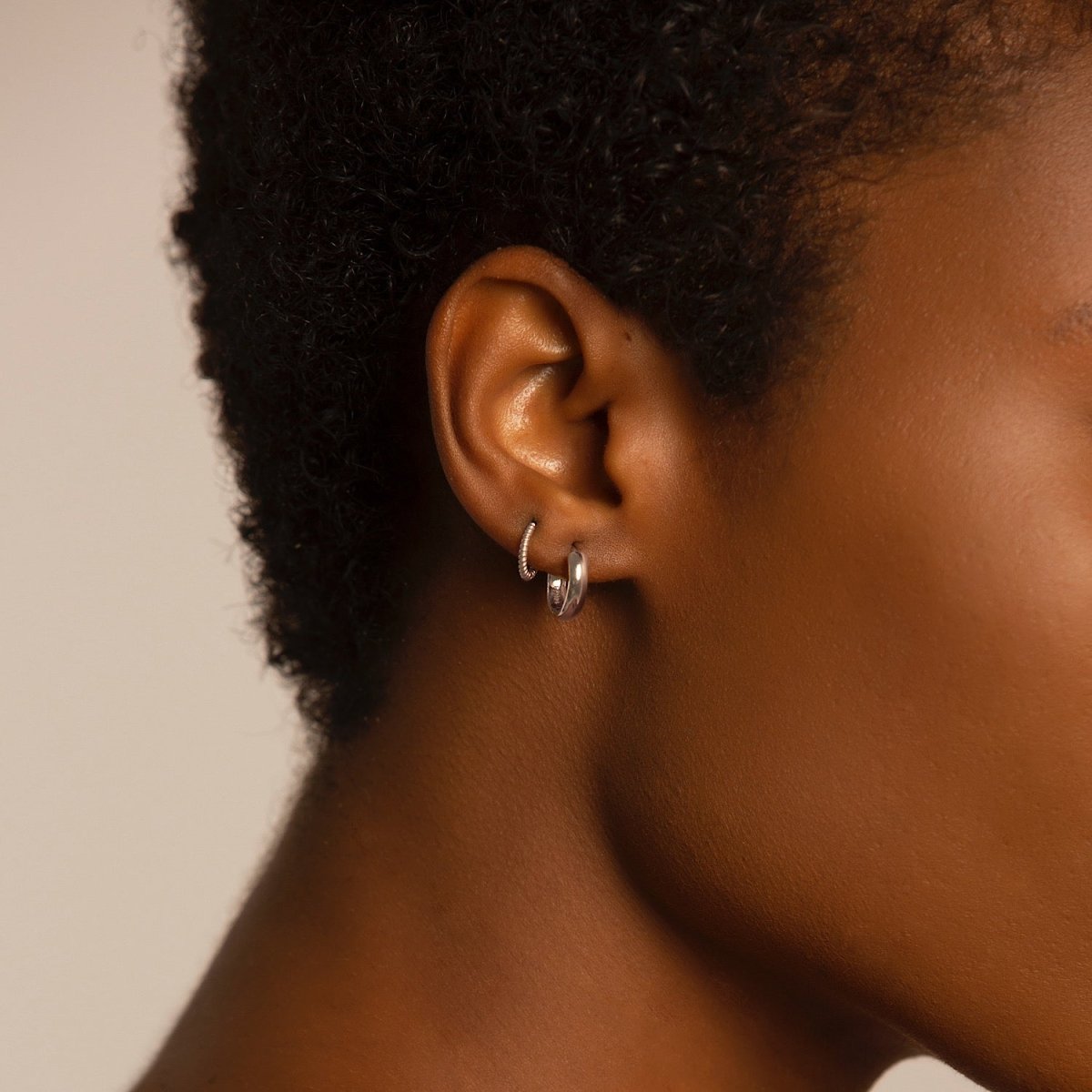 Close-up of woman's ear featuring Amyo Jewelry's White Gold Texture Rope Huggie Hoop Earrings and 14K White Gold Boiyfriend Mini Hoops. 