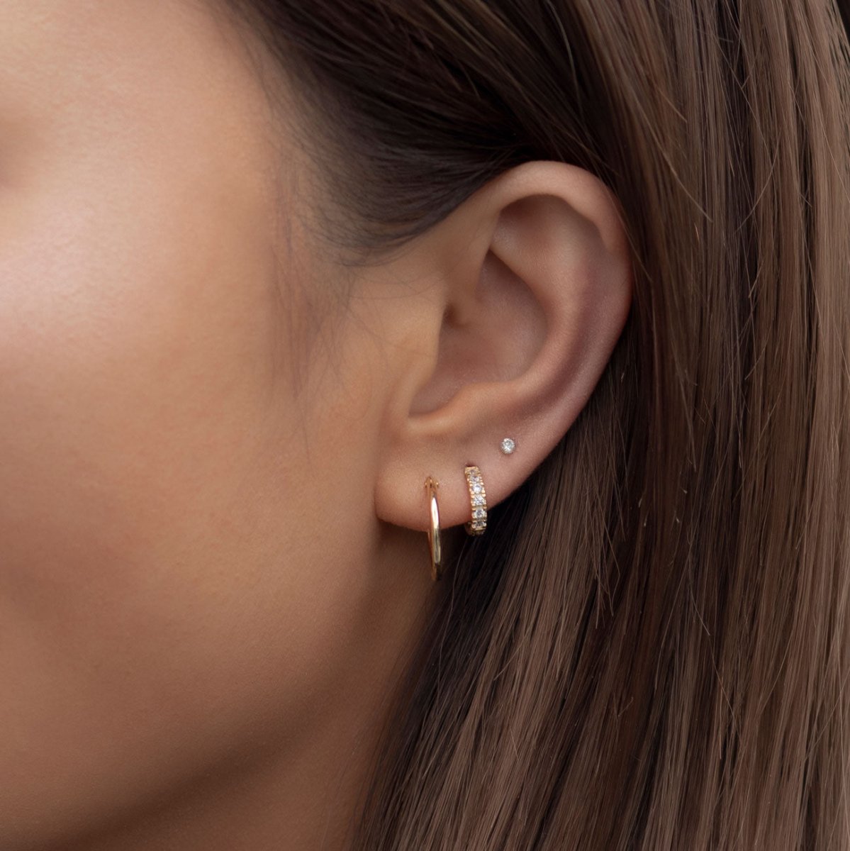 Close-up of woman's ear featuring Tiny 14K Gold Crystal Stud Earrings Paired with Huggie Earrings 