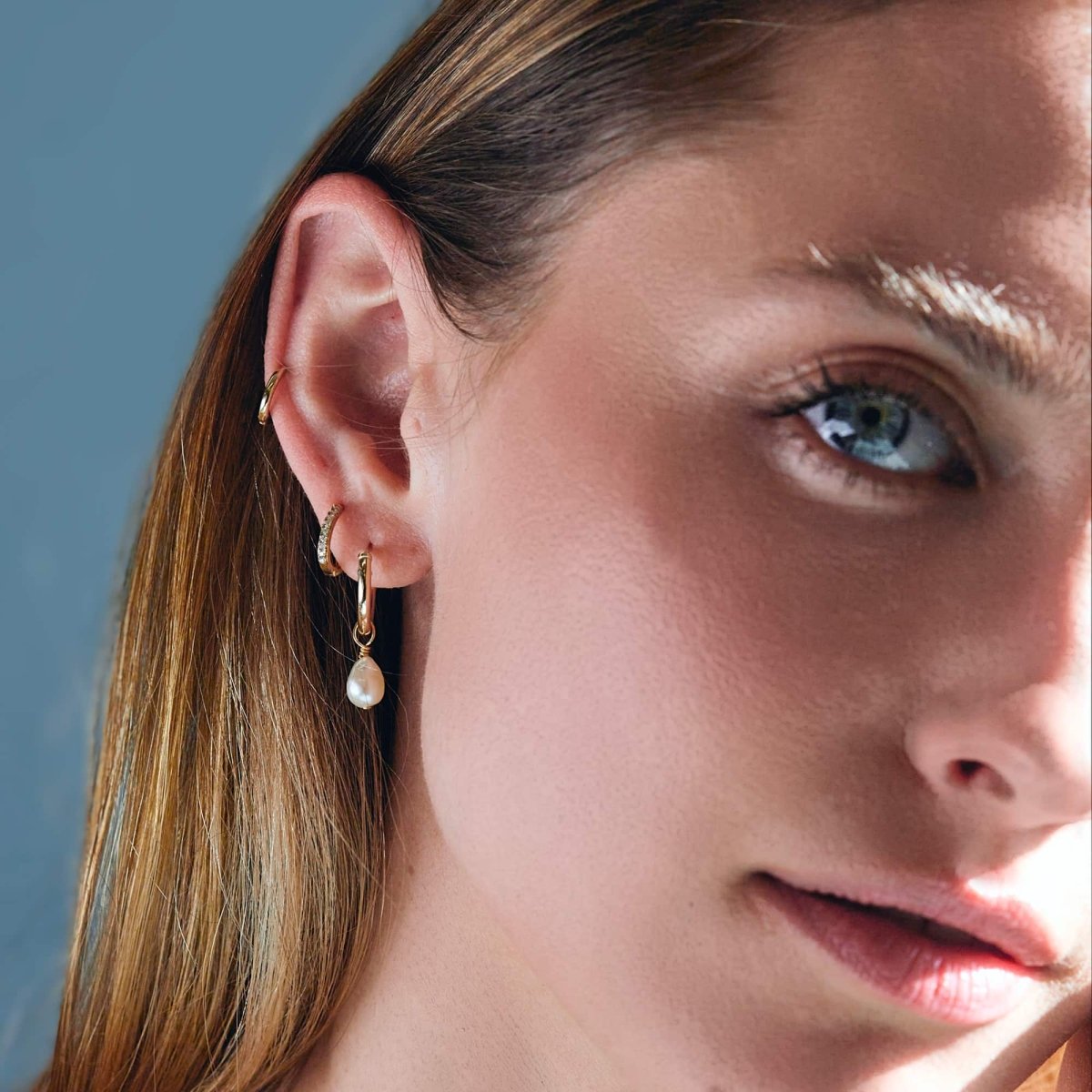 Close-up of woman's frontal side profile featuring 14K Gold Single Thin Pave Huggie paired with Pearl Drop Hoop Earrings. 