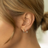 Close-up of woman's ear featuring 14K White Gold Thin Huggie Single Hoop and 14K White Gold Midi Hoop Earrings. 