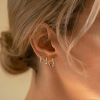 Close-up of woman's ear featuring 14K Solid White Gold Tri Baguette Huggie Hoops Moissanite Crystal, 14K Midi Hoop Earrings, and 14K Pave Rope Huggies 