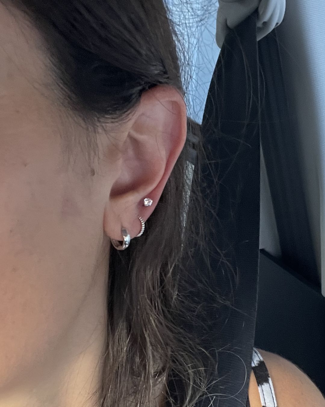 Close-up of a worn ear with a small silver crystal stud above two silver huggie hoops in the lobe